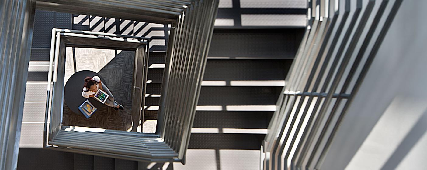 student seated at bottom of stairwell using ipad